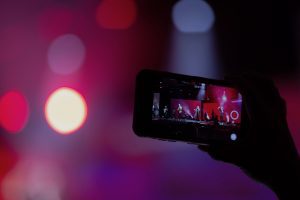 Person holding up a smart phone filming a band performing on stage